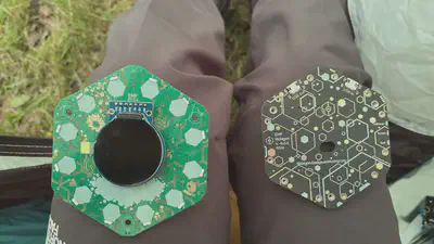 The same two hexagonal PCBs but turned over, revealing plant designs and a screen on the left PCB