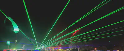 Photo of a black sky with multiple green laser beams spreading out from two central sources at the bottom