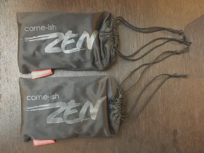 An image of two fabric pouches on a table. The pouches have a stylized “Corne-Ish Zen” printed on them.